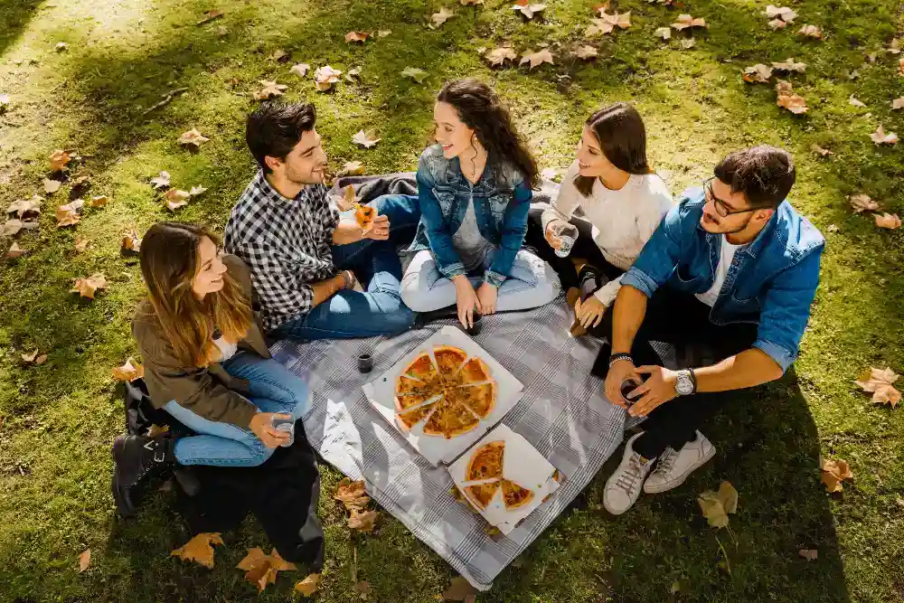 a group of people sitting on a blanket eating pizza