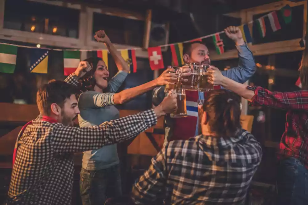 Group of people celebrating and toasting with beer mugs in a lively pub